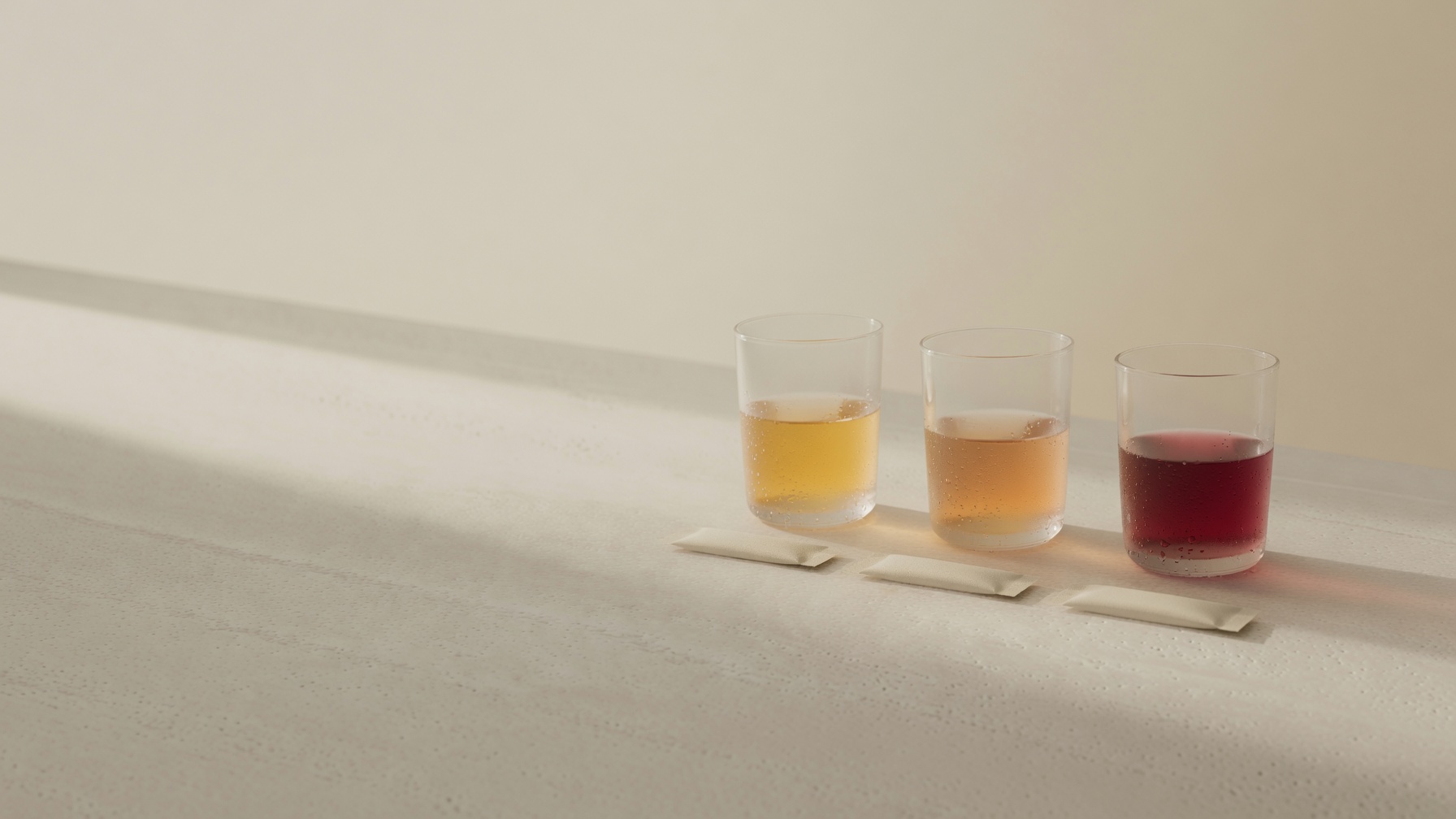 Trois verres — or, ambre, rose profond — dans la lumière du matin sur pierre de travertin